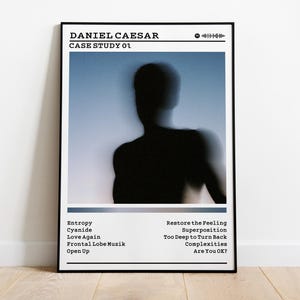 May include: A framed poster featuring the album art for Daniel Caesar's "Case Study 01." The image shows a blurred silhouette of a person against a blue and white gradient background. The poster includes the album title, artist name, and tracklist.