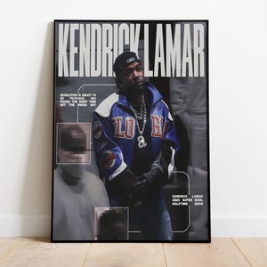 May include: A framed poster featuring Kendrick Lamar. The poster has a black frame and displays a photo of Lamar wearing a blue and white jacket. Text includes "Kendrick Lamar" and text about the Super Bowl Halftime Show.