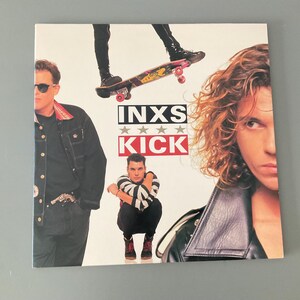 May include: Album cover for INXS's "Kick" featuring band members and a skateboarder. The album title is in bold red letters with the band's name above. The cover has a white background with the band members in various poses.