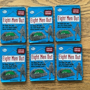 May include: Six packs of "Eight Men Out" baseball cards. Each pack is blue with the title in white and red, and features a baseball player illustration. The text reads "The Black Sox and the 1919 World Series Movie Baseball Cards".