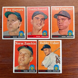 May include: Five vintage baseball cards featuring Washington Senators players. Each card has a portrait of a player, with their name and position printed on the card. The cards are set against an orange background.