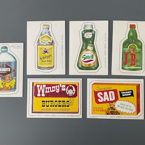 May include: A collection of six vintage Crazy Labels trading cards featuring various products. The cards are colorful and feature illustrations of a bottle of bleach, a bottle of tonic water, a bottle of cleaning solution, a bottle of alcohol, a fast food restaurant, and a box of trash bags.