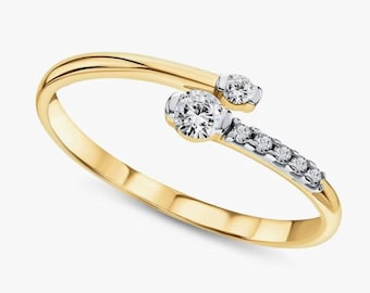 May include: A gold-tone ring with a bypass design. The ring features two larger, round, clear gemstones and a row of smaller gemstones. The ring's band is a polished gold color, and the gemstones are set in a silver-tone metal.