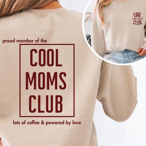 Puede incluir: Sudadera beige con el texto "COOL MOMS CLUB" en borgoña. El diseño está en la espalda y una versión más pequeña en la parte delantera. También se incluyen los textos "proud member of the" y "lots of coffee & powered by love".