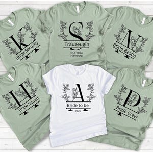 Könnte beinhalten: Eine Sammlung hellgrüner und weißer T-Shirts mit schwarzem Text und floralen Designs. Die Shirts zeigen Sätze wie "Bride Security", "Bride Squad", "Bride Bestie" und "Bride Crew". Ein Shirt sagt "Bride to be 2026."