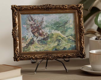 May include: A framed painting of a ship at sea in a storm. The painting is in a gold ornate frame and is displayed on a small metal easel. The artwork depicts a ship tossed in turbulent green and white waves.