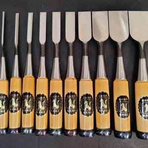 May include: A set of ten wood chisels with yellow handles and silver blades. The blades vary in width and shape. Each handle has a black and gold label with a stylized image. The chisels are arranged in a row.