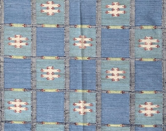 May include: Blue and light blue woven rug with a geometric pattern. The rug features a grid design with alternating squares of solid blue and patterned squares with white and red accents. The text "RugMania Creations" is visible.