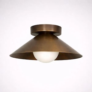 May include: A bronze-colored ceiling light fixture with a conical shade and a round, white globe light. The fixture has a circular base and a wide, downward-sloping shade. The overall design is modern and minimalist.