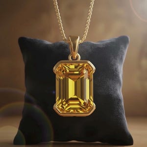 May include: A gold pendant necklace featuring a large, rectangular yellow gemstone. The pendant is set in a gold frame and hangs from a delicate gold chain. The necklace is displayed on a black pillow.