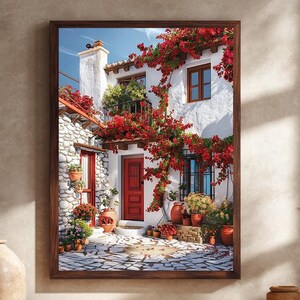 May include: A framed print of a charming Mediterranean scene. A white stucco building with a red door and window frames is adorned with vibrant red flowers. Terra cotta pots with plants line the entrance and windows. The scene is set on a stone-paved courtyard.