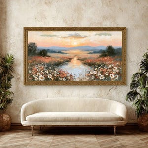 May include: A rectangular landscape painting in a gold frame depicting a sunset over a meadow with a central stream. The scene features white wildflowers in the foreground, rolling hills in the distance, and a soft orange and blue sky.