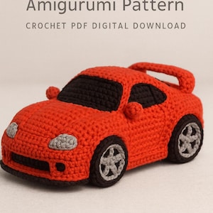 May include: A red crocheted sport car amigurumi with black windows, grey headlights, and grey wheels. The text reads Sport Car Amigurumi Pattern CROCHET PDF DIGITAL DOWNLOAD at the top and bottom of the image, describing a digital crochet pattern.