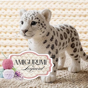 Op de afbeelding: Een handgemaakte amigurumi luipaardwelp, gemaakt van wit garen met donkerbruine vlekken. Het gehaakte dier heeft een gedetailleerd gezicht en staat. De afbeelding bevat een label met de tekst "AMIGURUMI Leopard".