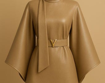 May include: A tan-colored leather top with a high neckline and wide sleeves. The top is cinched at the waist with a matching belt featuring a gold-colored buckle. The garment is displayed on a mannequin against a neutral background.