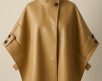 May include: A tan-colored cape-style jacket with a high collar and two dark buttons. The jacket features short sleeves with decorative flaps and two dark buttons on each sleeve. The garment is displayed on a mannequin.