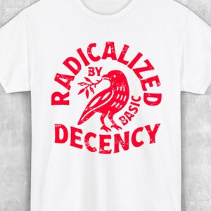 Könnte beinhalten: Weißes T-Shirt mit roter Grafik, die "RADICALIZED BY BASIC DECENCY" um einen Vogel mit einem Zweig herum zeigt. Das Shirt hat auch Werbetext in Rot.