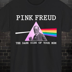 Op de afbeelding: Zwart t-shirt met de tekst "PINK FREUD" boven een afbeelding van Sigmund Freud in een roze driehoek, met een regenboog en de tekst "THE DARK SIDE OF YOUR MOM".