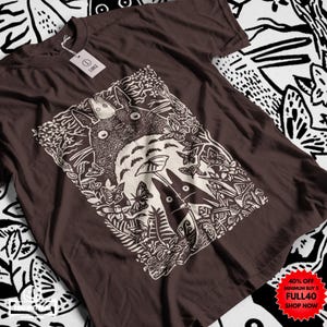 Pu&ograve; includere: T-shirt marrone con grafica bianca di una scena di foresta con due personaggi dei cartoni animati e farfalle. La maglietta ha un'etichetta attaccata. L'angolo in basso a destra dell'immagine ha un adesivo promozionale rosso e giallo con la scritta "40% OFF MINIMUM BUY 5 FULL40 SHOP NOW".