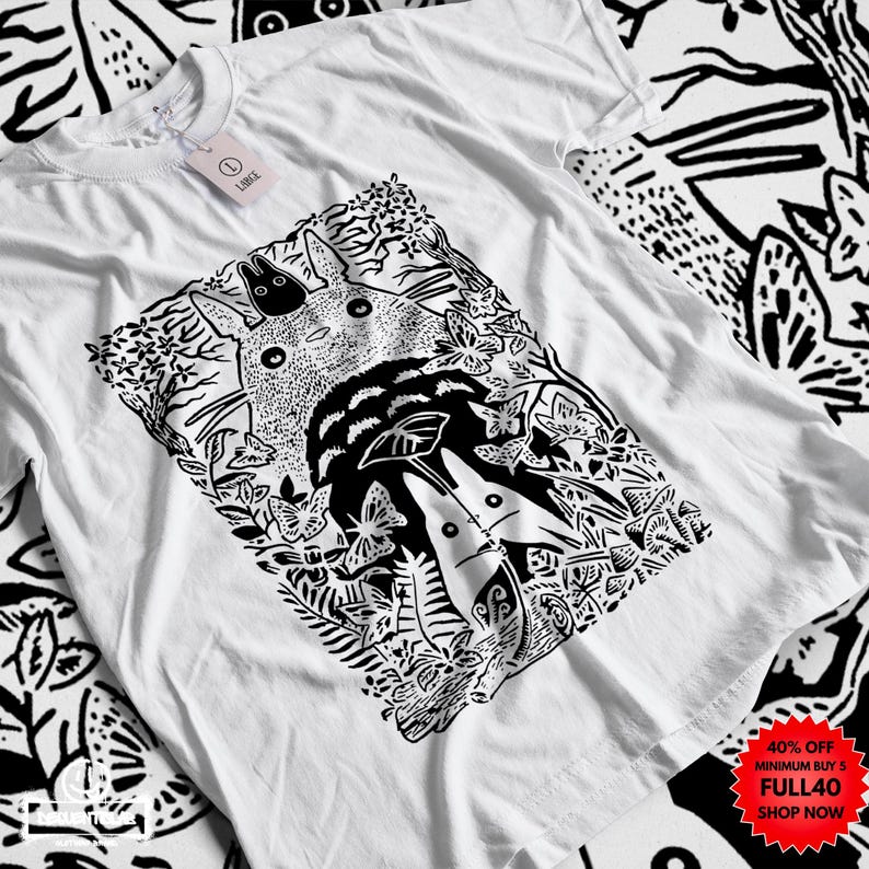 Pu&ograve; includere: T-shirt bianco con grafica in bianco e nero di una scena forestale con una grande creatura rotonda e creature pi&ugrave; piccole. Il design include farfalle e fogliame. La maglietta ha scollo tondo e maniche corte.