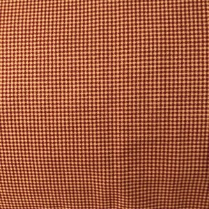 May include: Close-up of a fabric with a small, repeating gingham pattern. The pattern features a dark red color on a cream background, creating a classic and textured look. The fabric is likely used for clothing or home decor.
