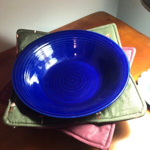 May include: A deep blue ceramic bowl with a swirling pattern sits on top of two fabric coasters. The coasters are green and brown with a mushroom pattern.
