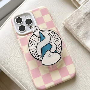 May include: A pink and white checkered phone case with a clear pop socket featuring a cartoon snake design. The snake is white with a blue body and is set against a black and white maze background.