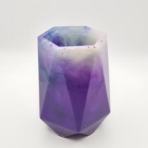 May include: A geometric, multi-faceted container in shades of purple, white, and blue. The container has a hexagonal top and base, with a gradient effect. The object is likely a decorative vase or pencil holder.