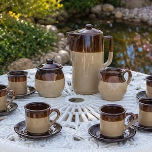 Peut inclure: Un service à thé en céramique comprenant une grande verseuse, un sucrier avec couvercle, un petit pot à lait et six tasses assorties avec soucoupes. Chaque pièce présente un design bicolore avec une partie supérieure marron et une base beige.