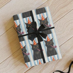 May include: Gift wrapping paper featuring a repeating pattern of black cats wearing party hats and smoking pipes, set against blue and white striped backgrounds. A wrapped gift with a black bow is in the center. Additional wrapping paper and ribbon are also visible.