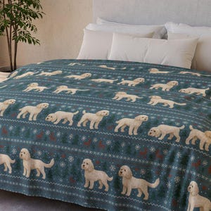 Op de afbeelding: Een teal fleece deken met een herhaald patroon van crèmekleurige honden, sneeuwvlokken en decoratieve elementen. De deken is gedrapeerd over een bed met witte kussens en een grijs hoofdbord. De kamer heeft een neutraal kleurenschema.