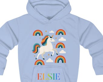 May include: A light blue hooded sweatshirt featuring a unicorn design with rainbows and clouds. The unicorn has a white body, a colorful mane and tail, and a golden horn. The name "ELSIE" is printed in rainbow colors on the front.