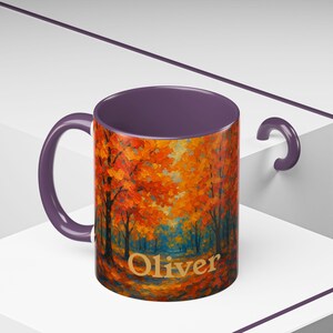 Puede incluir: Taza de cerámica con una vibrante escena de bosque otoñal en tonos naranja, rojo y azul. La taza tiene un interior y asa morados, con el nombre "Oliver" impreso en la parte delantera.
