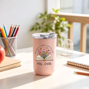 May include: A pink insulated tumbler with a white lid. The tumbler features a floral design with an open book and the text "Teach them, love them, watch them grow" and "Mrs. Smith". A red apple, pencils, and a notebook are also visible.