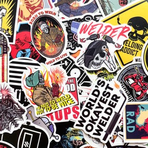 May include: A collection of colorful stickers with welding-themed designs. The stickers feature skulls wearing welding helmets, sparks, and text like "Born to Weld" and "World's Okayest Welder". The color palette includes red, yellow, black, and white.