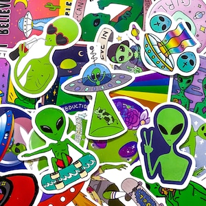 Può includere: Una collezione di adesivi colorati con alieni verdi in varie pose. Alcuni alieni vanno sullo skateboard, altri sono in navicelle spaziali. Gli adesivi includono testo come "BELIEVE" e "ABDUCTION".