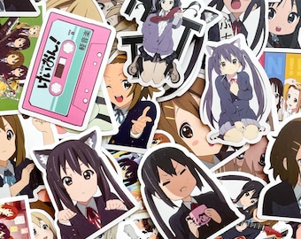 Pode incluir: Uma coleção de adesivos em estilo anime com vários personagens e designs. Os adesivos apresentam personagens com olhos grandes, e alguns têm orelhas de gato. Um adesivo é uma fita cassete rosa com texto japonês.