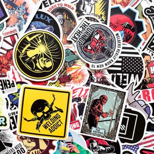 May include: A collection of colorful stickers with welding-themed designs. The stickers feature images of welders, welding tools, and text like "Welding Addict" and "Born to Weld". The stickers are in various shapes and sizes.