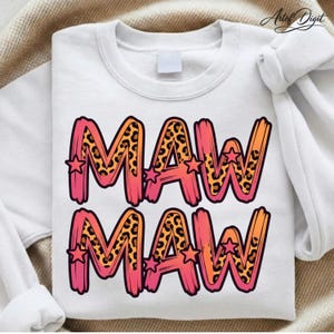 Peut inclure: Sweat-shirt blanc avec le mot "MAW" en grandes lettres colorées. Les lettres sont bordées de rose et d'orange, avec un motif léopard à l'intérieur. De petites étoiles sont placées autour des lettres. Le sweat-shirt est de style décontracté.