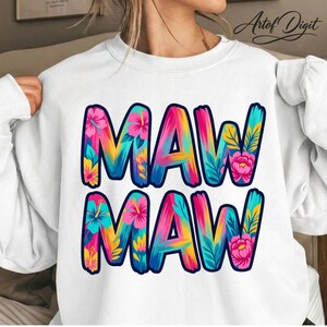 以下が含まれることがあります： 「MAW MAW」の文字が大きくカラフルなトロピカルテーマで描かれた白いスウェットシャツ。文字は青で縁取られ、ピンク、黄色、ティールブルーの花と葉のフローラルパターンで埋められています。