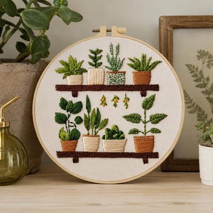 以下が含まれることがあります： 棚に飾られた鉢植えの植物を詳細に描いた、丸い刺繍枠。植物は緑と茶色の色合いで表現され、鉢はテラコッタとベージュです。背景はニュートラルな生地です。