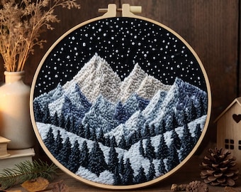 Könnte beinhalten: Ein runder Stickrahmen mit einer handgestickten Landschaft aus schneebedeckten Bergen und einem dichten Wald aus dunklen Tannen vor einem schwarzen Nachthimmel voller weißer französischer Knoten als Sterne, eingefasst in einen hellen Holzrahmen.