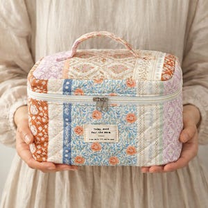 May include: A quilted cosmetic bag with a handle, featuring a patchwork design in various colors and patterns. The bag includes a zipper closure and a small label with text. The overall aesthetic is vintage and floral.