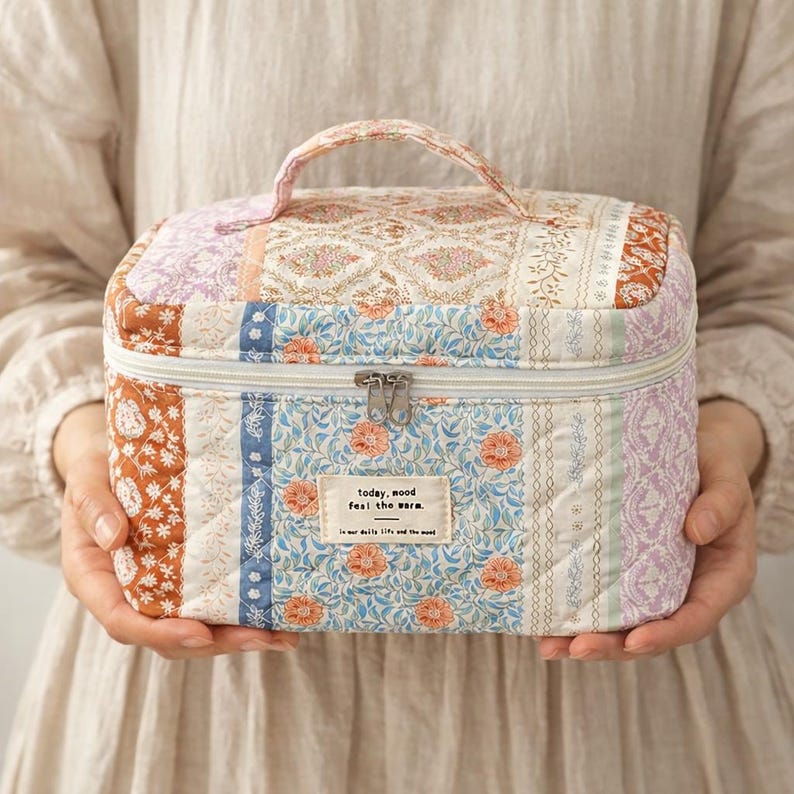 May include: A quilted cosmetic bag with a handle, featuring a patchwork design in various colors and patterns. The bag includes a zipper closure and a small label with text. The overall aesthetic is vintage and floral.