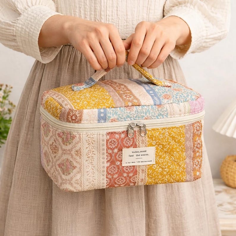 May include: A quilted cosmetic bag with a patchwork design in shades of yellow, pink, blue, and cream. The bag has a zipper closure, a handle, and a small label that reads "today, mood feel the warm."