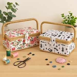 Pode incluir: Duas caixas de costura com alças tecidas. Uma caixa apresenta um padrão floral com rosas rosa e vermelhas em um fundo branco. A outra tem um padrão em preto e branco com tema de costura. Perto estão carretéis de linha, tesouras e botões.