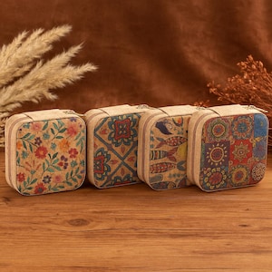 Può includere: Quattro portagioie quadrati in sughero con chiusure a zip. Ogni custodia presenta un design unico: motivi floreali, geometrici, di pesci e patchwork. Le custodie sono realizzate in sughero e sono esposte su una superficie di legno.