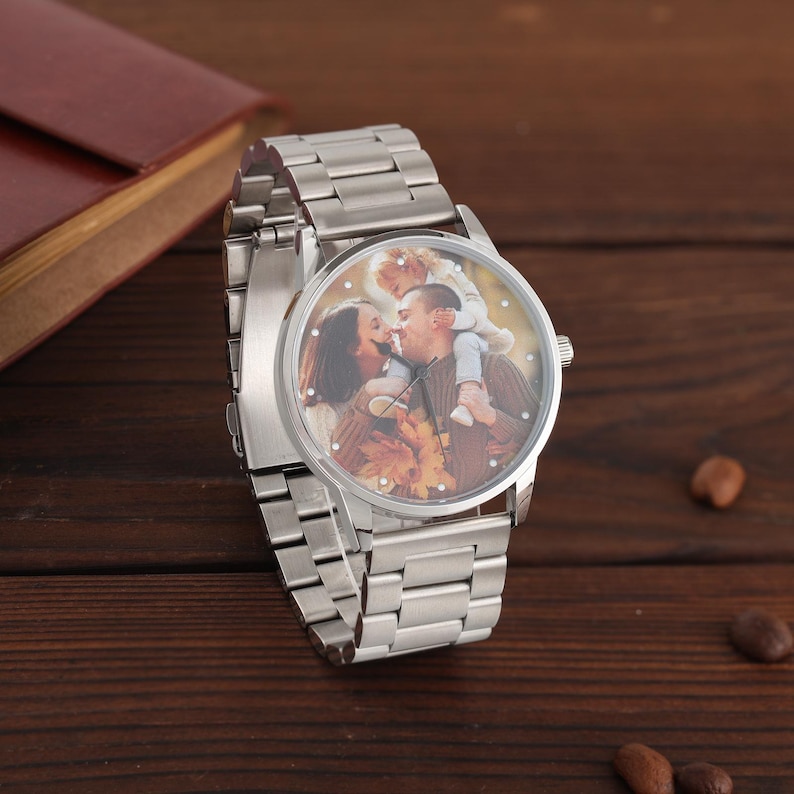 May include: A silver wristwatch featuring a family photo on the watch face. The watch has a stainless steel strap and a round face. The photo shows a couple kissing with a child on the man's shoulders.