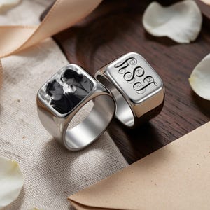 May include: Two silver-toned metal rings with square faces. One ring features a black and white engraved photograph of two people. The other ring displays an engraved black script monogram with the letters h, S, and J in a decorative font style.