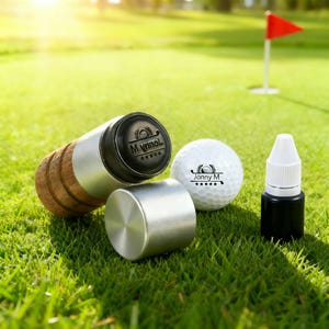 May include: A golf-themed set on green grass, including a golf ball with "Jonny M" text, a cylindrical metal and cork item with "Myrnol" text, and a small black bottle with a white cap. A red flag is in the background.